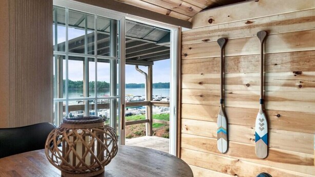 A wooden interior with a round table and a decorative lantern, a view of the outdoors through a glass door, and three paddles on the wall.