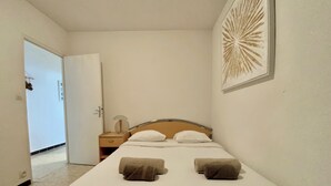 A neatly made bed with two pillows and two towels, a bedside table with a lamp, and a wall art piece. - TELLINES - Appartement  avec petite vue mer (Le Grau-du-Roi)