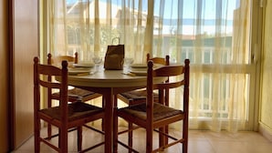 Un comedor con una mesa redonda, cuatro sillas de madera y una ventana con cortinas traslúcidas.