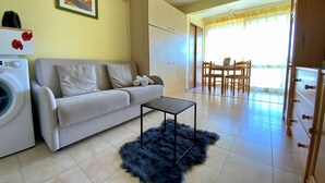 Una sala de estar con sofá, mesa de centro, lavadora y comedor con sillas y mesa.