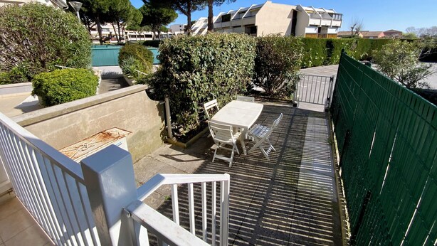 Un patio con una mesa y sillas, una cerca verde y una piscina al fondo.