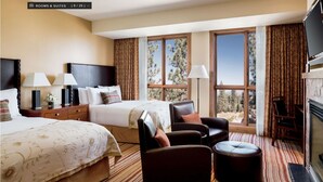 Habitación de hotel con dos camas, un sofá, una silla, chimenea y ventanas amplias con vista a árboles.