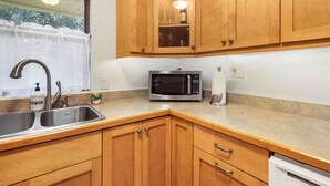 A kitchen with wooden cabinets, a stainless steel sink, a microwave, and a window with a curtain. - Quiet & Close to hospitals, UF and more (Gainesville)