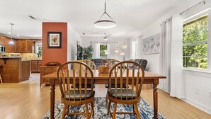 Un comedor con una mesa y sillas de madera, un tapete azul estampado y una cocina al fondo.