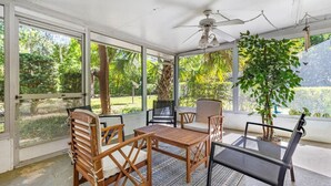 Un espacio de estar al aire libre cubierto con muebles de madera, un ventilador de techo y vistas a un jardín exuberante.