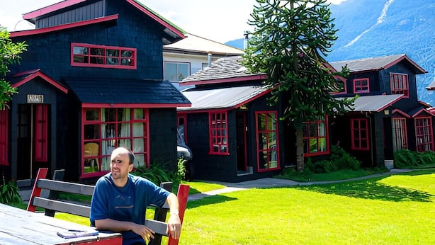 A person sitting on a bench outside a house with a dog nearby. - Quelen Austral (Hualaihué)