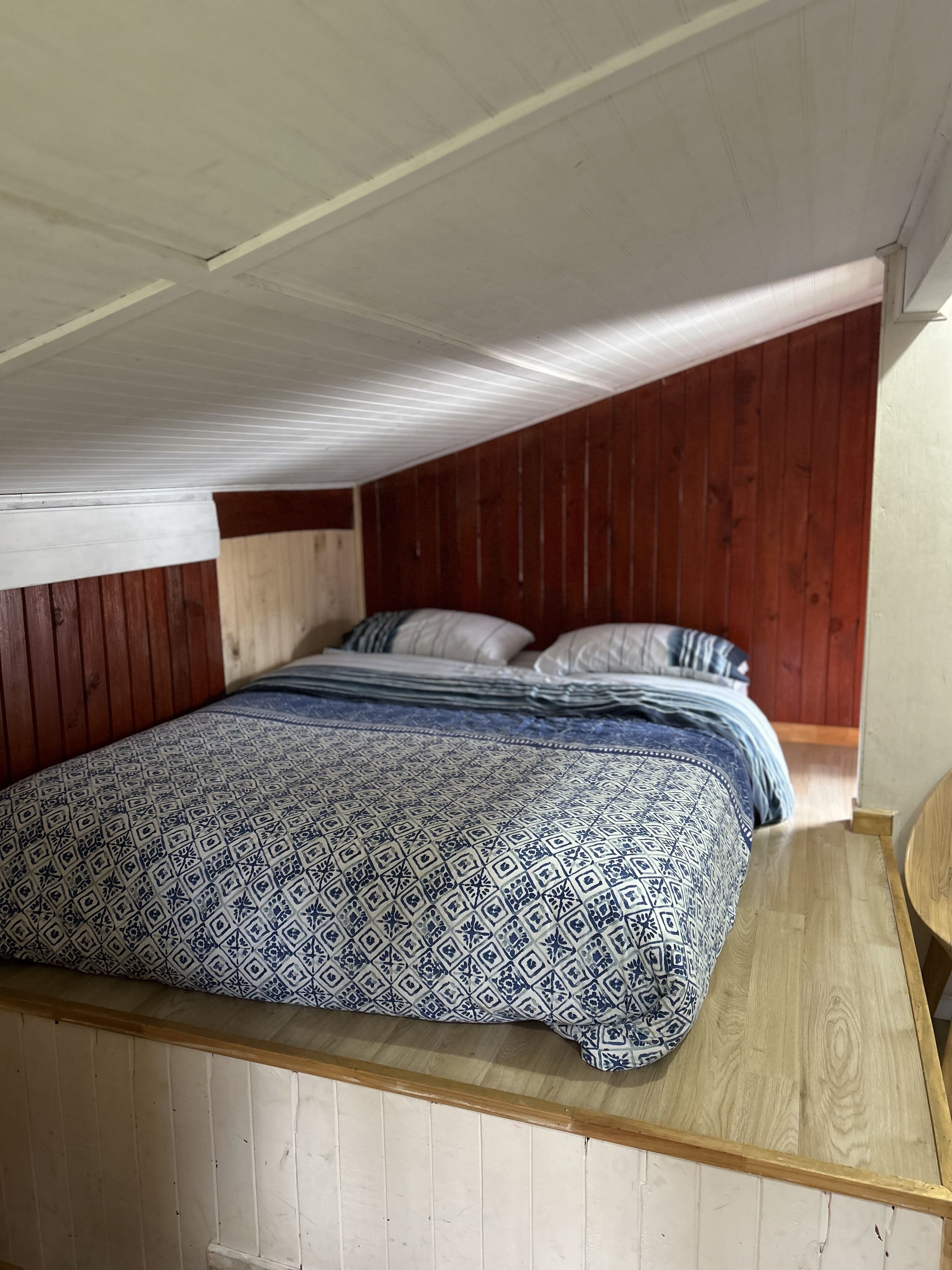 A bedroom with a sloped ceiling, wooden walls, and a bed with patterned bedding.