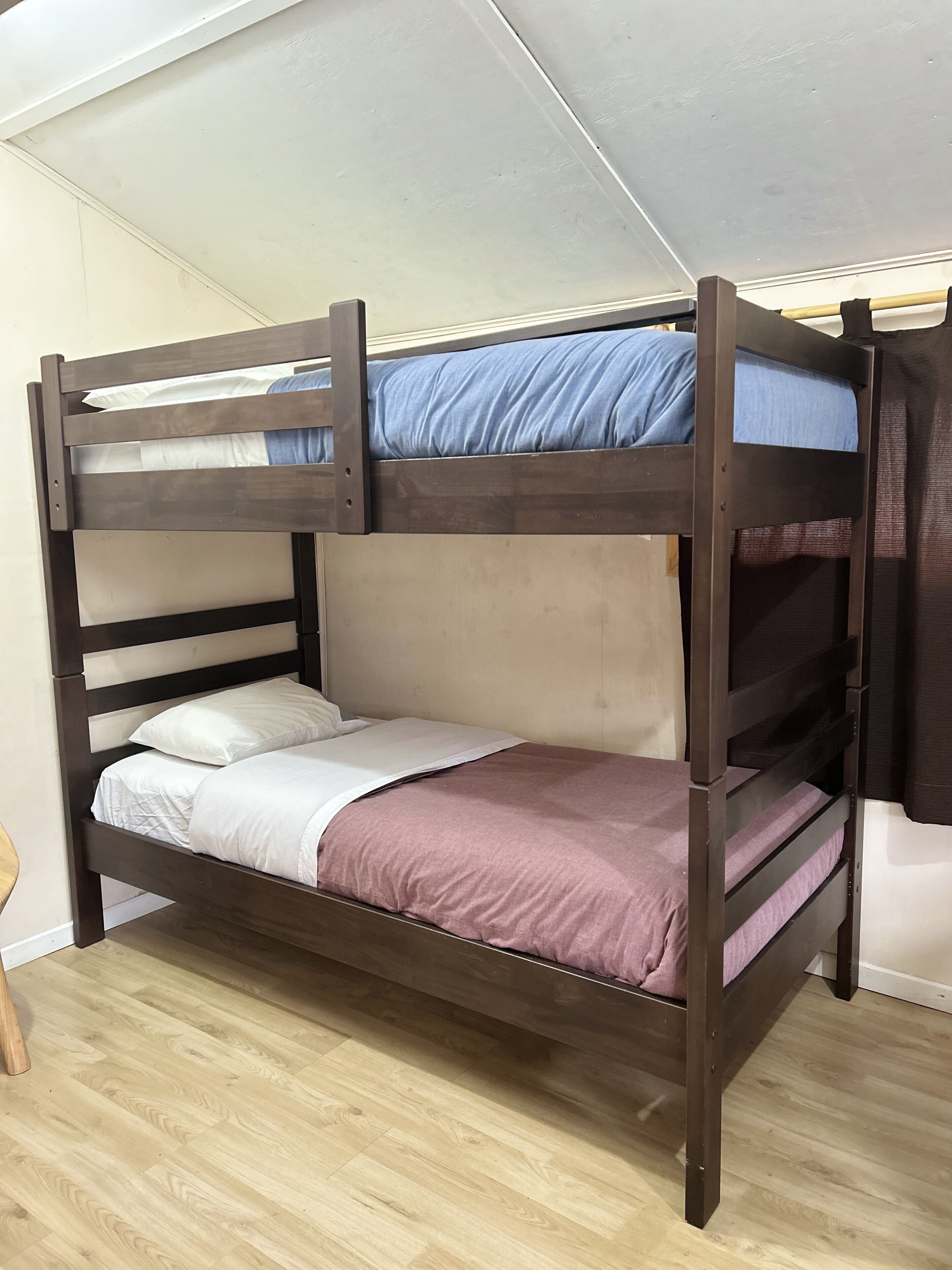 Een stapelbed met twee verhogingen, houten frame en een hoofdbord.