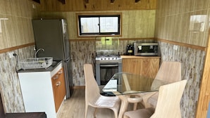 A compact kitchen with a refrigerator, stove, microwave, and wooden cabinets. - Quelen Austral (Hualaihué)