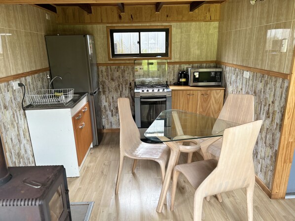 A compact kitchen with a refrigerator, stove, microwave, and wooden cabinets. - Quelen Austral (Hualaihué)
