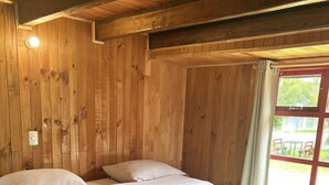 A wooden-paneled room with a bed, pillows, and a neatly folded towel on the bed. - Quelen Austral (Hualaihué)