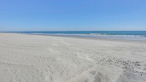 En bred, sandet strand med fodaftryk, der fører ned mod vandet.