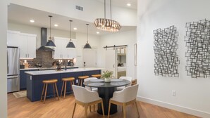 A modern kitchen with a central island, pendant lighting, and a dining area with a round table and chairs.