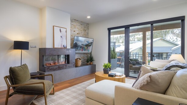 A modern living room with a fireplace, comfortable seating, a television, and a large window offering a view of a mountain landscape.