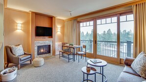 A spacious living room with a fireplace, comfortable seating, a television, and large windows offering a view of the outdoors. - Pet-Friendly Cle Elum Condo - Hike, Ski & Relax! (Cle Elum)