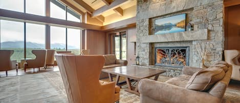 Un salón espacioso con chimenea de piedra, muebles de cuero y grandes ventanales con vistas a la montaña.