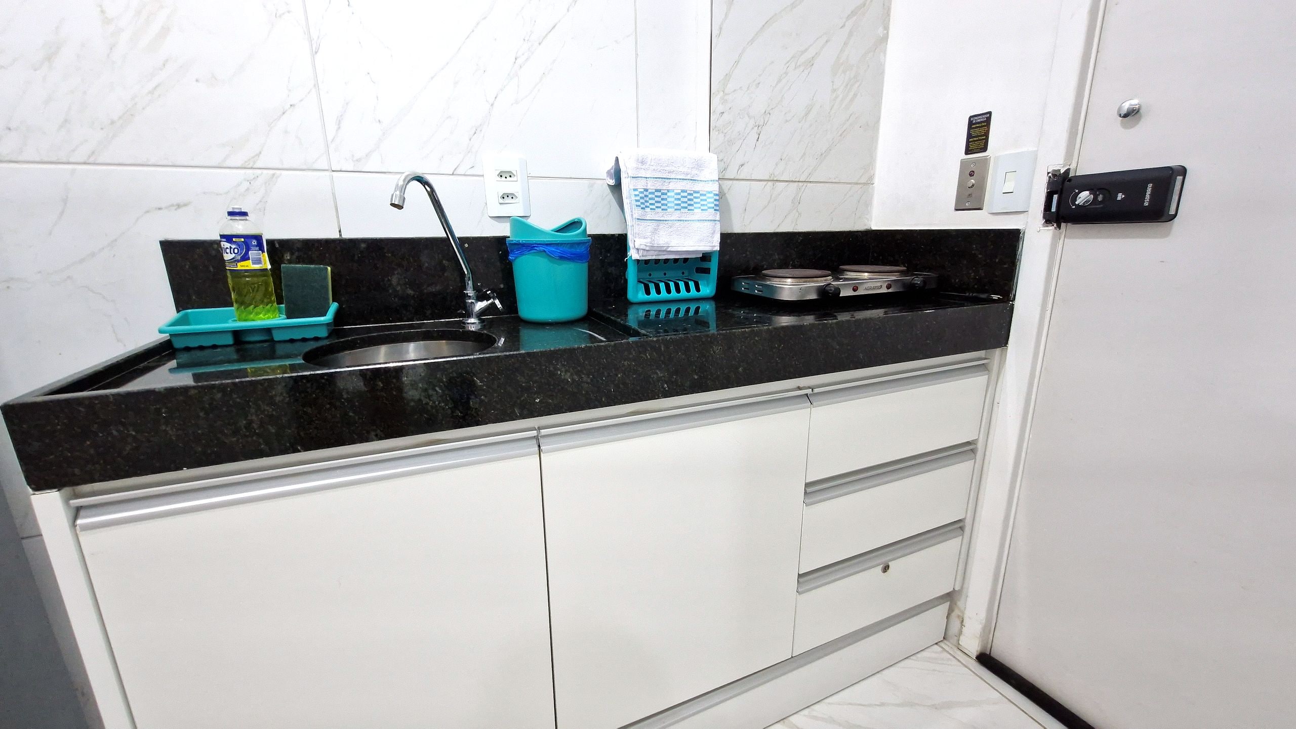 A kitchen with a black countertop, white cabinets, a sink, a stove, and various kitchen items.