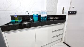 A kitchen with a black countertop, white cabinets, a sink, a stove, and various kitchen items.