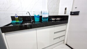 Una cocina con encimera negra, armarios blancos, un lavamanos, una estufa y diversos utensilios de cocina.