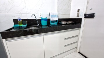 Una cocina con encimera negra, armarios blancos, un lavamanos, una estufa y diversos utensilios de cocina.