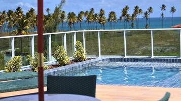 A pool area with a view of palm trees and the ocean.