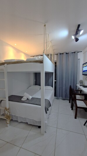 A bunk bed room with a desk and chair, a computer, and a window with curtains.