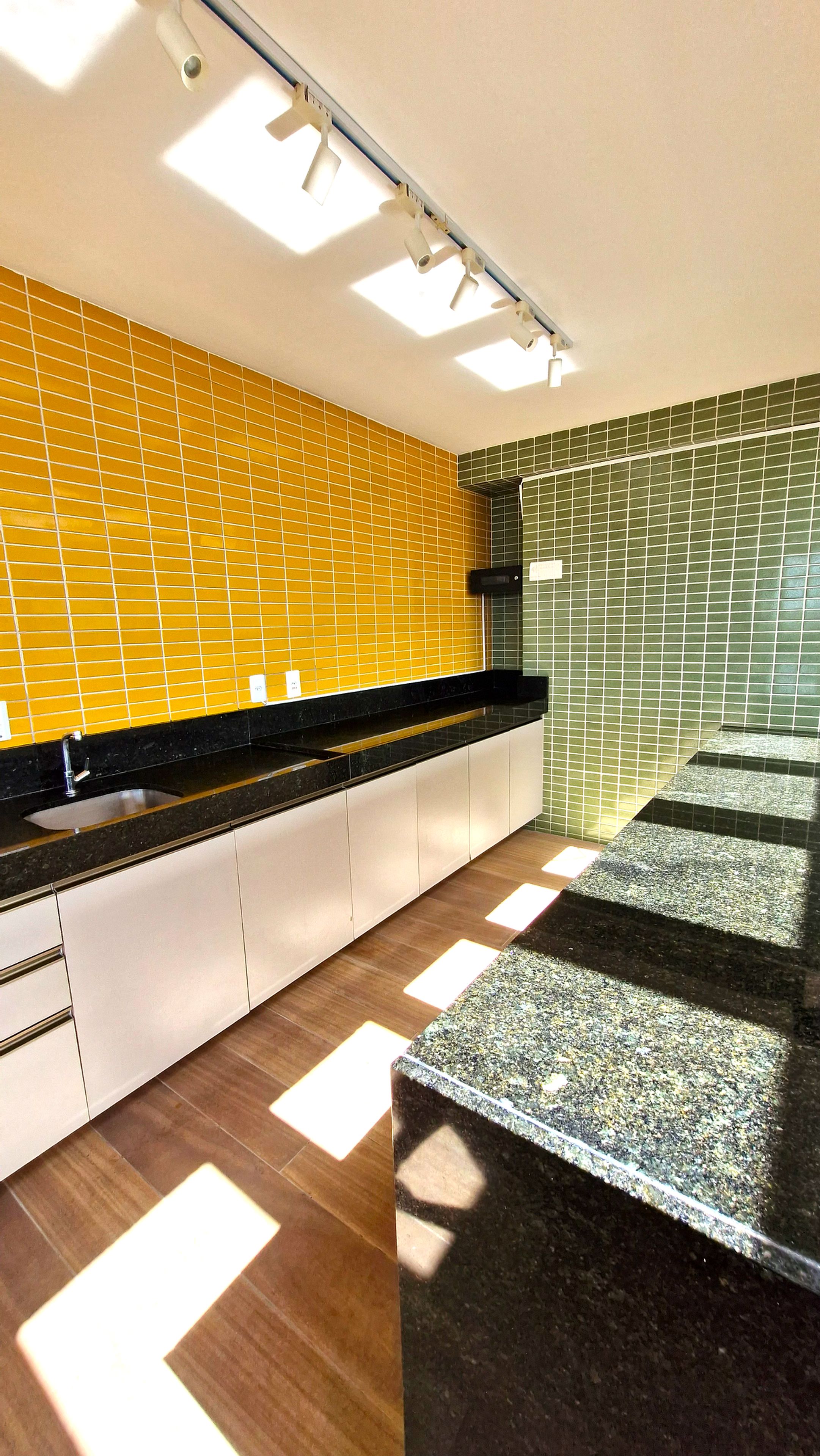 A modern kitchen with a black countertop, yellow and green tiled backsplash, and a wooden floor.