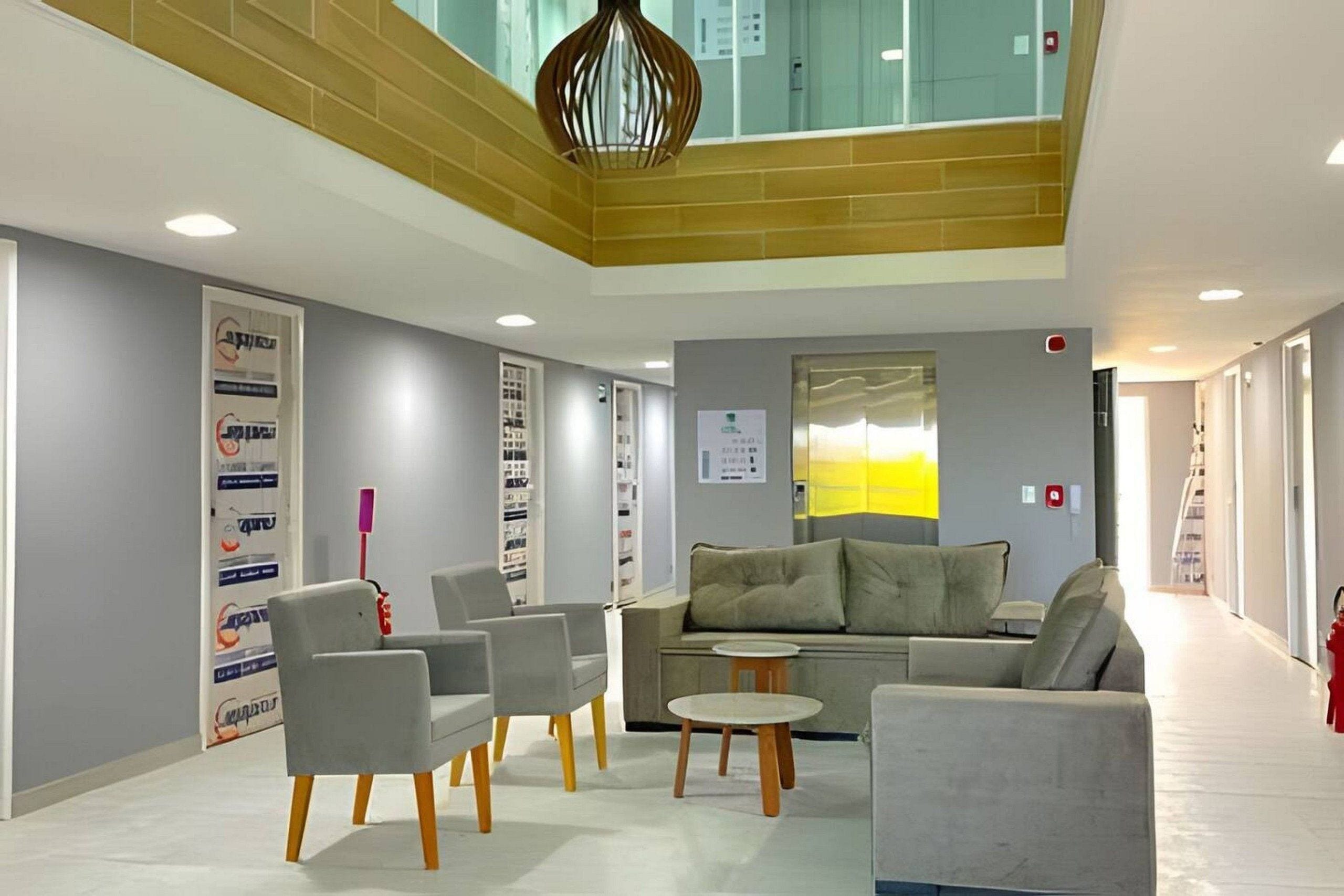 A modern lobby with a high ceiling, grey sofas, and a central table.