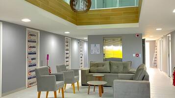 A modern lobby with a high ceiling, grey sofas, and a central table.
