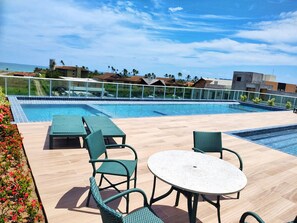 Un área de piscina en la azotea con vistas despejadas al océano, una piscina y sillones de descanso.