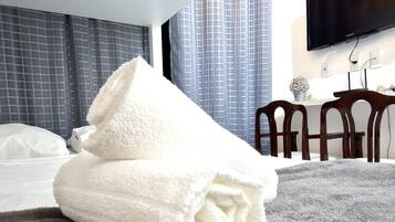 A neatly made bed with a folded white towel, a grey textured rug, and a modern room with a flat-screen TV mounted on the wall.