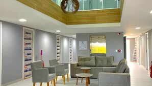 A modern lobby with a high ceiling, grey sofas, and a central table.