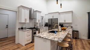 A modern kitchen with white cabinetry, a central island with stools, a stainless steel refrigerator, and a gas stove.