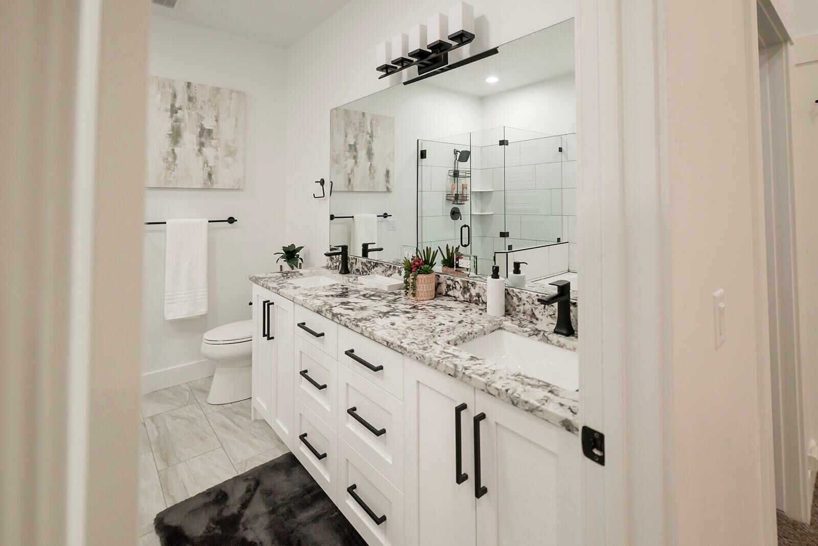 Un baño moderno con encimera de mármol, muebles blancos y un espejo grande.