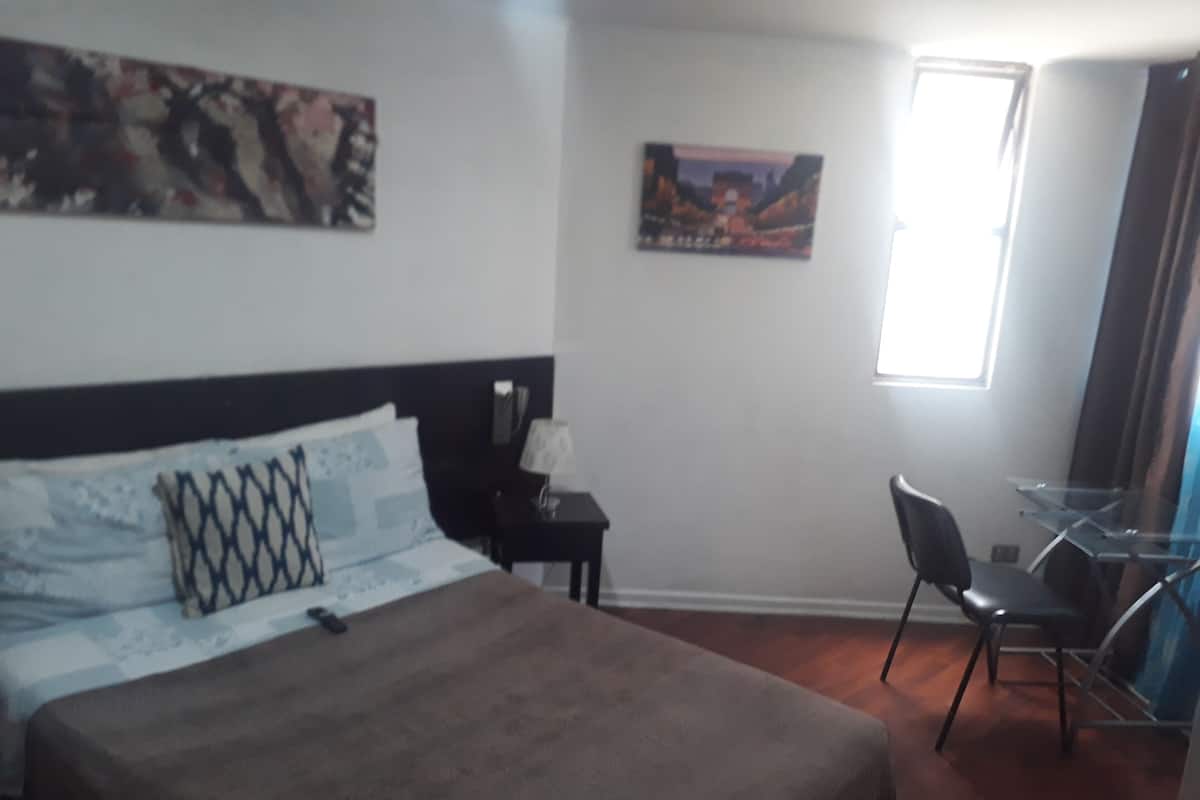 Una habitación de hotel con una cama, un escritorio, una silla y dos cuadros en las paredes.