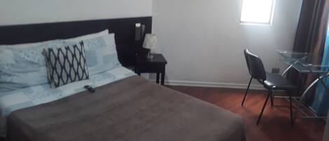 A hotel room with a bed, a desk, a chair, and two paintings on the walls.