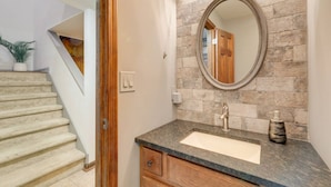 Un baño con pared de piedra, un espejo redondo, un lavamanos y un mueble de madera.
