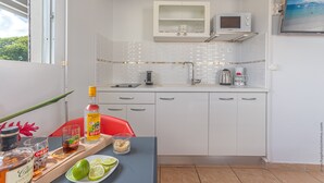 Cocina compacta con armarios blancos, microondas y cafetera. Se observa una mesa de comedor con una bandeja de bebidas y gajos de lima.