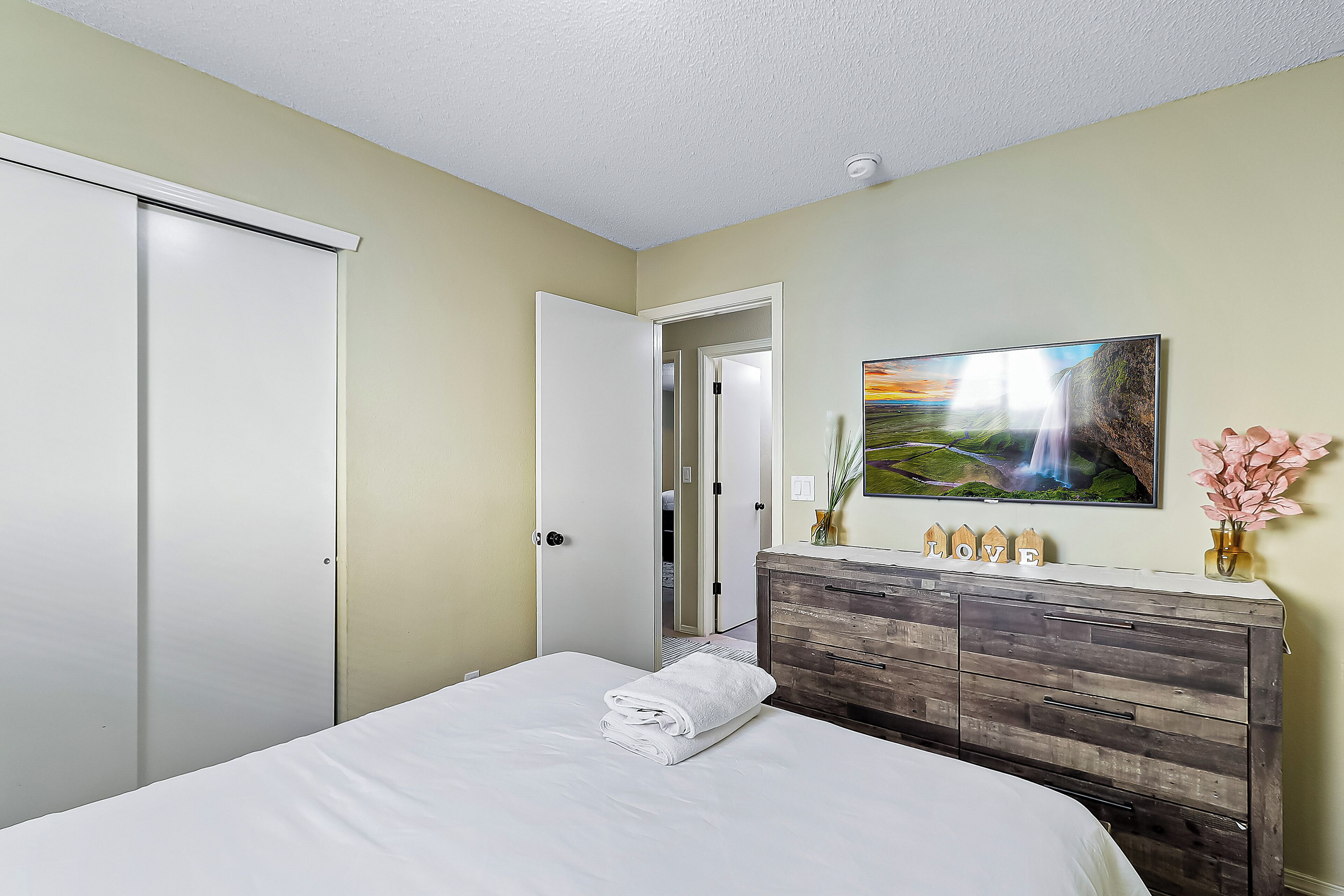 Une chambre à coucher avec un lit, une commode, un tableau et une porte donnant sur une autre pièce.
