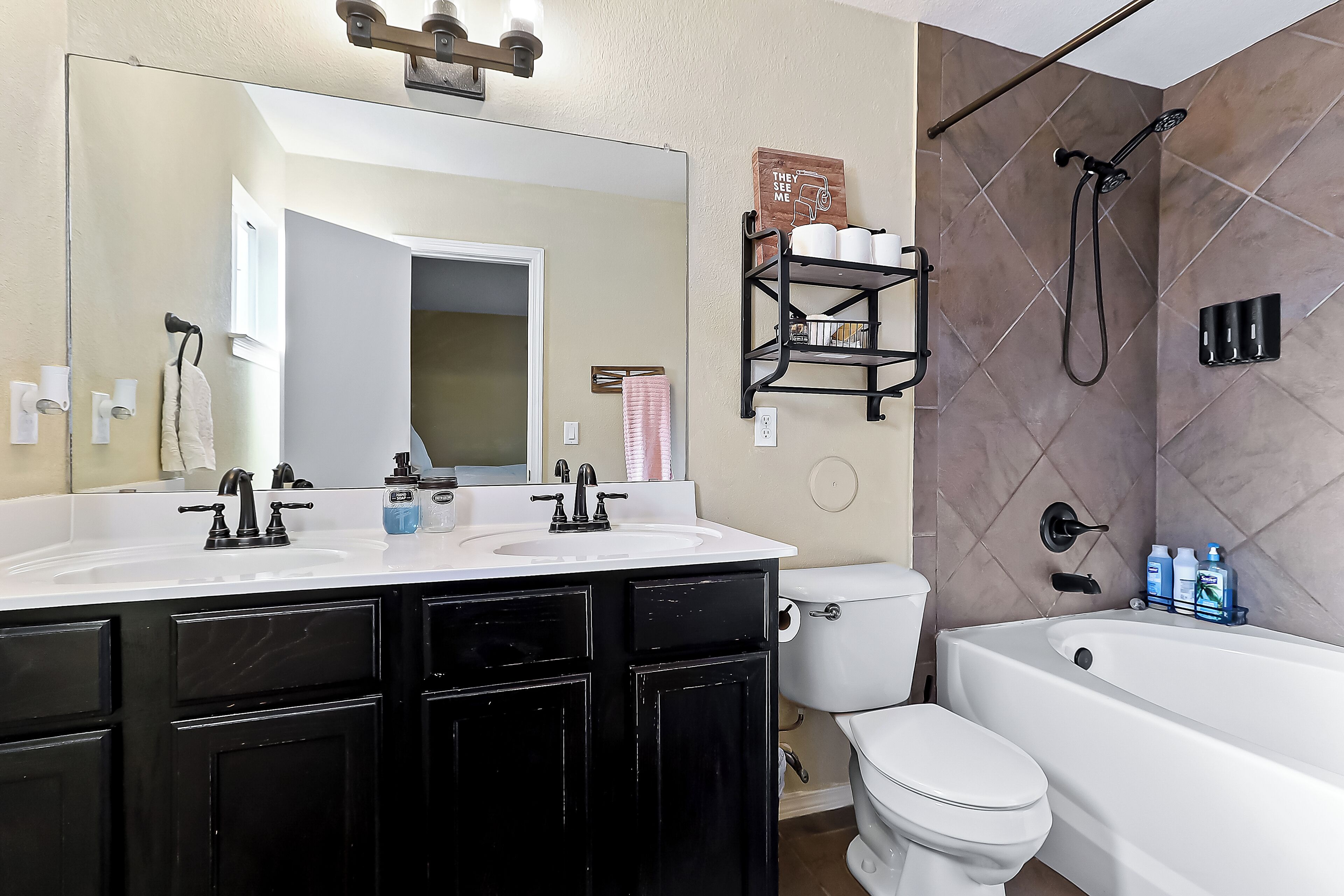 A bathroom with a white sink, black cabinets, a large mirror, a toilet, and a bathtub.
