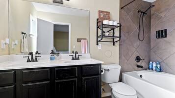 A bathroom with a white sink, black cabinets, a large mirror, a toilet, and a bathtub.