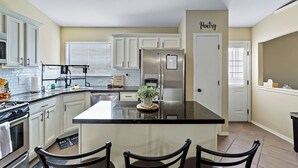 A kitchen with white cabinets, a stainless steel refrigerator, a black countertop island, and a door labeled "Pantry". - Cozy Farm House Home Located Near Main Freeways SUPER HOST on other platforms  (El Paso)