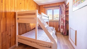 Una cama individual superpuesta en una habitación con paredes de madera y una ventana con cortinas.