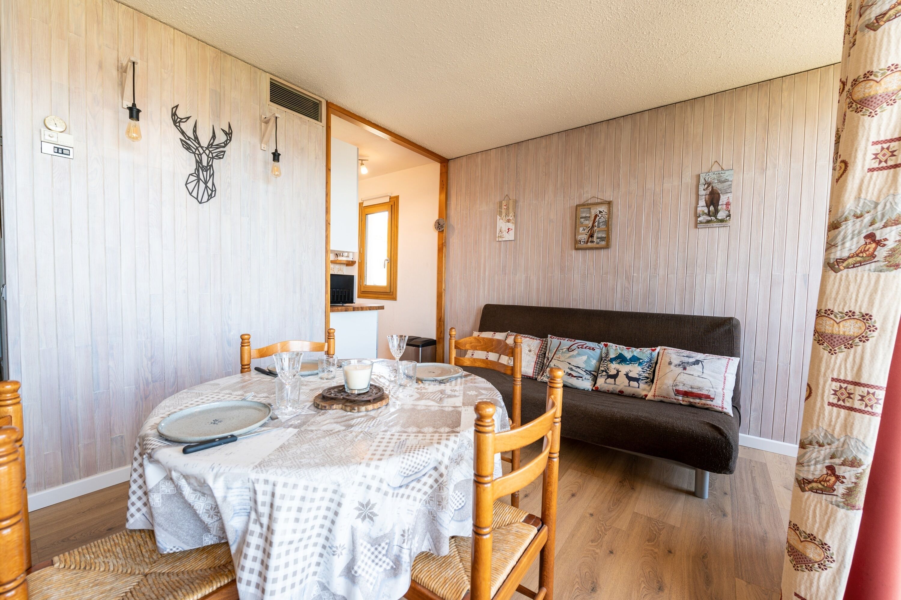 Una stanza accogliente con un tavolo da pranzo apparecchiato per due, un divano con cuscini decorati e una parete adornata con elementi decorativi a tema animali.