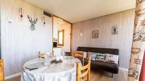 Una habitación acogedora con una mesa de comedor lista para dos personas, un sofá con cojines estampados y una pared decorada con motivos de animales.
