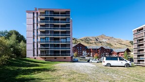 Un hotel de varios pisos con balcones, un área de estacionamiento y montañas al fondo.