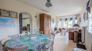 Un comedor con una mesa redonda cubierta con mantel verde y blanco, sillas de madera y un aparador de madera.