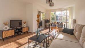 A modern living room with a sofa, TV, and dining area. - Place Cosy - Charmant appt pour 4 (Courcouronnes)