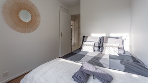 A bedroom with a bed, a round mirror, and a door leading to another room. - Place Cosy - Charmant appt pour 4 (Courcouronnes)