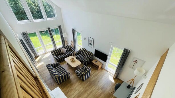 Amplia sala de estar con sofás a rayas, una mesa de centro y un televisor de pantalla plana. Ventanas amplias ofrecen vistas al exterior.